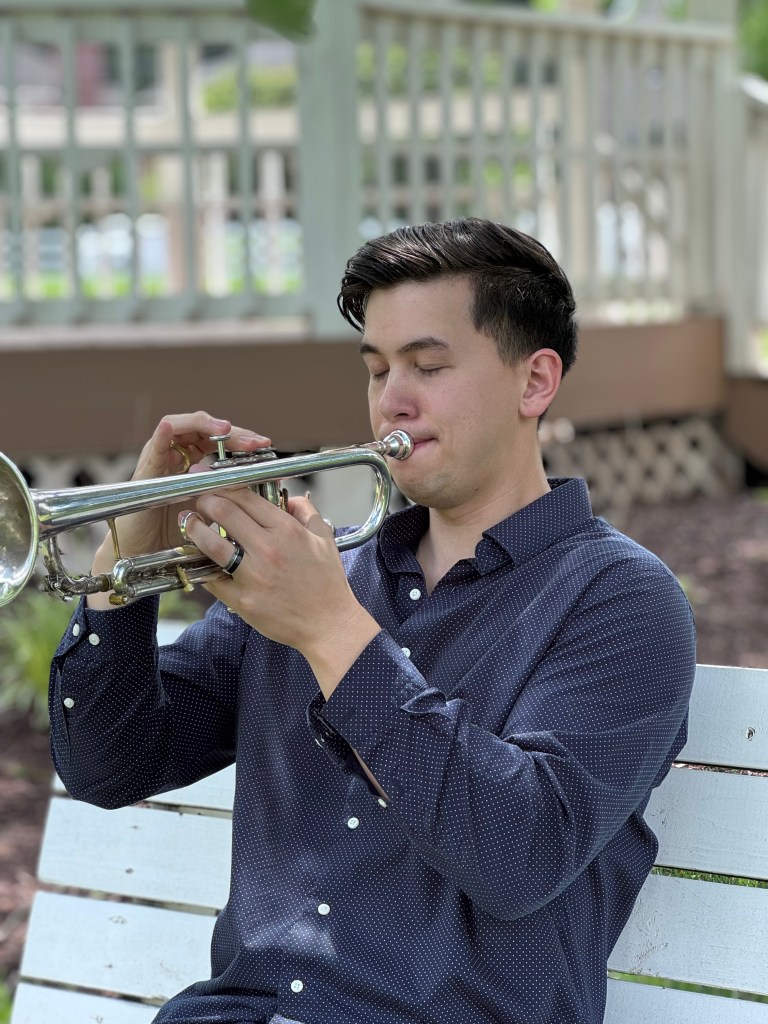 Ben Rattanavong raising his trumpet to his face, ready to perform in a park.
