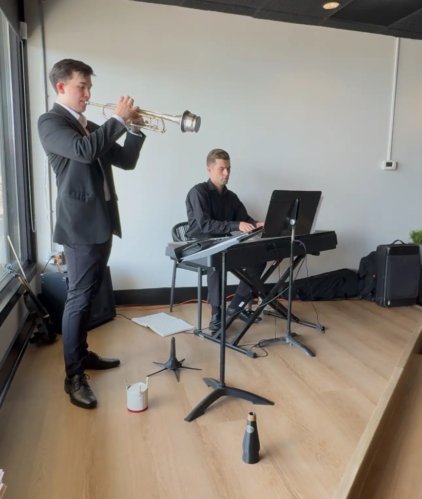 Trumpet player in a suit performing alongside pianist on stage